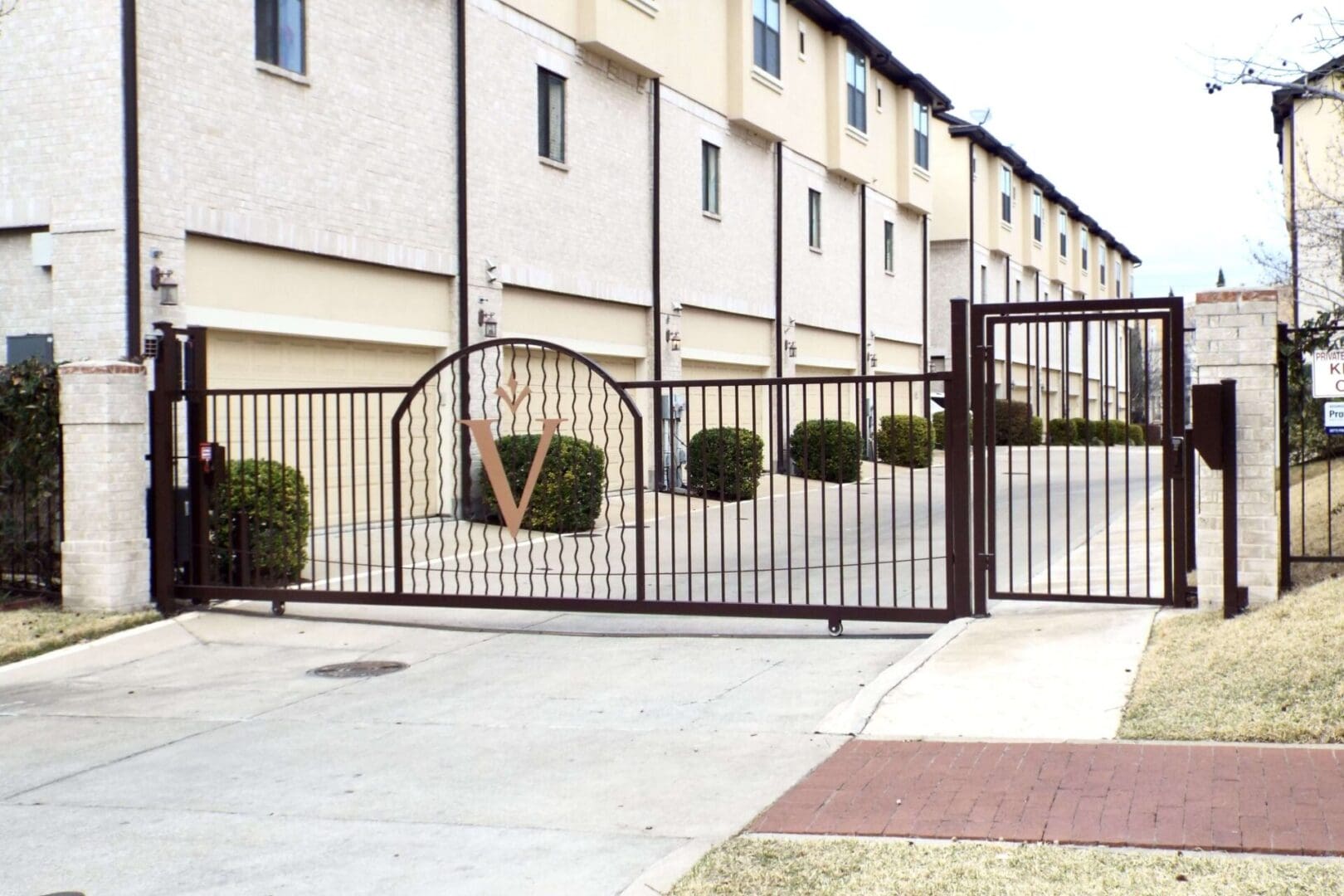 A gated driveway with a metal fence and bushes.